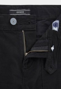 Pantaloni in denim nero con chiusure a cerniera e bottone. Presentano un'etichetta cucita, hardware metallico e una texture liscia.