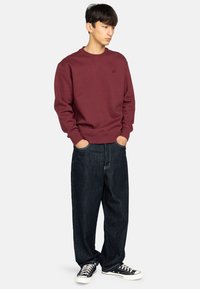 Bordeaux sweatshirt met geribbelde manchetten en zoom, gecombineerd met losse donkere spijkerbroeken en zwarte sneakers met witte zolen.