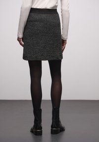 Musta teksturoidu hame, jossa on istuva vyötärönauha, polvipituinen malli ja hienovarainen kuviointi. Yhdistetty mustiin nilkkureihin ja läpikuultamattomiin sukkahousuihin.