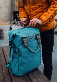 Modrý látkový batoh se šedými akcenty a dvojitými horními madly. Obsahuje logo vpředu, uzavření na zip a nastavitelné boční popruhy.