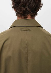Khaki jacka med avslappnad passform, med en vikbar krage, ryggsömsdetalj och en horisontell tygslinga vid nacken. Slät textur.