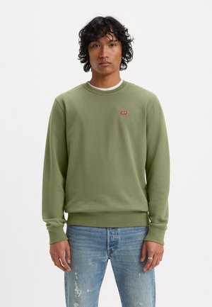 Green sweatshirt with crew neck and ribbed cuffs, featuring a small red Levi's logo on the chest. Worn with distressed blue jeans.
