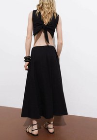 Ensemble noir en deux pièces comprenant un haut sans manches avec un nœud dans le dos et une jupe longueur cheville. Tissu lisse et silhouette décontractée.