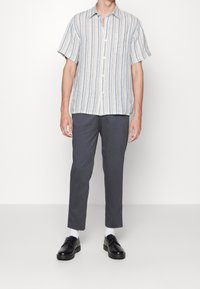 Košile s krátkým rukávem v světle modré a bílé barvě, kombinovaná s tmavě šedými padnoucími kalhotami a černými botami, s bílými ponožkami.