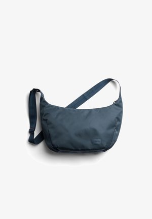 Sac à épaule bleu marine foncé en tissu lisse, doté d'une forme large, d'une sangle ajustable et d'un petit patch logo sur le devant.