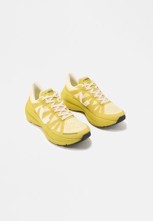 Paire de chaussures de course athlétiques jaunes avec des lacets blancs et un grand logo blanc "N" sur les côtés, sur un fond blanc uni.