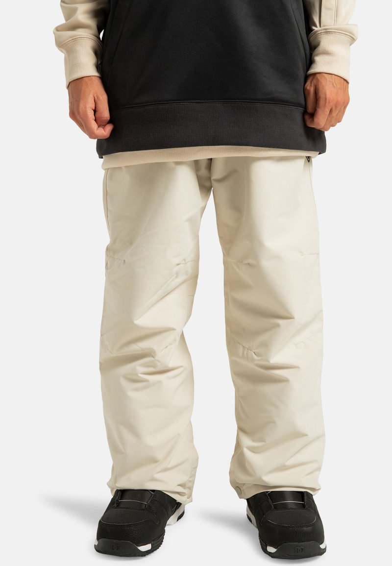 Lichtbeige waterdichte broek met een relaxte pasvorm, voorzien van zakken, ontworpen voor comfort, gecombineerd met zwarte sportieve schoenen.