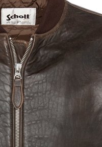 Veste en cuir marron avec fermeture éclair argentée et doublure matelassée, comportant une étiquette de marque Schott NYC à l'intérieur du col.