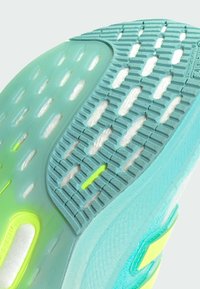Semelle de chaussure en aqua et vert clair ; présente un caoutchouc texturé avec des rainures et des découpes pour l'adhérence ; finition lisse sur les bords.