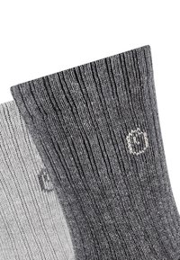 Calzini a maglia grigi e grigio chiaro con texture a coste, dotati di un piccolo logo circolare di colore contrastante sul lato.