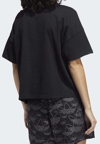 Svart oversized T-shirt med korta ärmar, med en enkel och slät yta. Bakstycket har en enkel design, ihop med mönstrade svarta shorts.