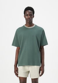 Green short-sleeve t-shirt made of cotton, featuring a round neckline with white and dark green stripes. Soft texture and relaxed fit.