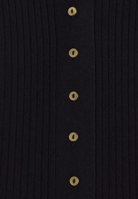 Schwarze Rippstrickjacke mit sieben goldfarbenen Knöpfen in der Mitte, die einen strukturierten Stoff mit vertikalen Linien hervorhebt.