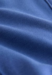 Gros plan sur un tissu bleu montrant une fine texture nervurée diagonale et des plis doux.