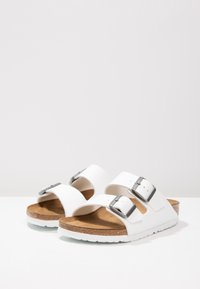 Sandali bianchi con due cinturini regolabili, fibbie argentate, plantare in sughero e suola in gomma bianca. Superficie superiore in sintetico liscio.