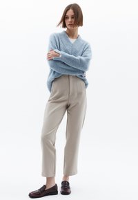 Lichtblauwe oversized gebreide trui met geribbelde textuur, gecombineerd met beige op maat gemaakte broek met voorplooien, en donkere loafers.
