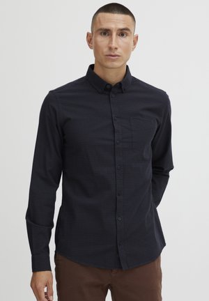 Dark blue checkered button-up shirt with long sleeves and a chest pocket, made from lightweight fabric, paired with brown trousers.