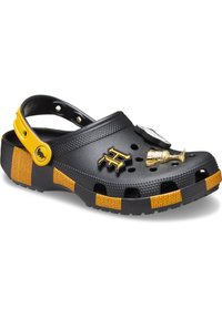Schwarzer Kunststoff-Clog mit einer gelb-schwarz gestreiften Sohle, dekorativen Charms, Belüftungsöffnungen und einem Fersenriemen für einen sicheren Sitz.