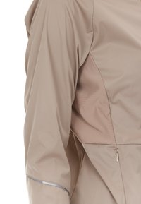 Ljusbeige jacka med en matt finish, som har ett mjukt tyg, en kontrasterande texturerad insats och detaljer med dragkedjeficka.