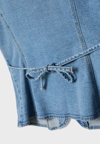 Svetlomodrá džínsovina s viditeľnými švami a uviazanou slučkou opasku vytvárajúcou mašľu v oblasti pása odevu.