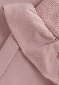 Lichtroze stof met een gladde textuur en een geraffineerde ruchedetail, gelaagd over een vlak, vergelijkbaar textured gedeelte van het materiaal.