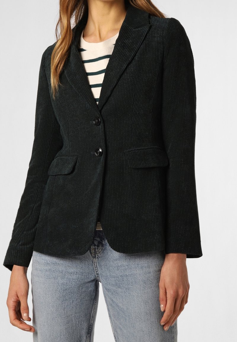 Blazer en velours côtelé vert foncé avec une coupe ajustée, fermeture à un bouton, deux poches avant et un tissu texturé. Associé à un jean bleu clair.