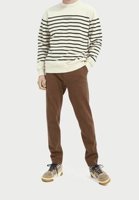 Sudadera de crema a rayas con líneas negras, pantalones de chándal marrones y zapatillas beige con acentos texturizados y cordones azul marino.