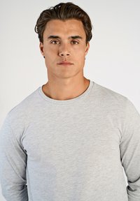 Vaaleanharmaa pitkähihaisen paita, joka on valmistettu pehmeästä kankaasta. Tässä paidassa on pyöreä kaula-aukko ja sileä, tasainen pinta. Ei näkyviä kuvioita tai koristeita.