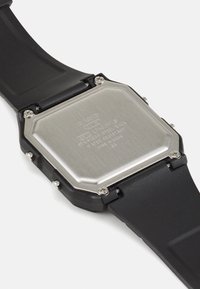 Montre bracelet en caoutchouc noir avec un cadran octogonal en acier inoxydable, présentant des détails gravés et des accents en métal argenté.
