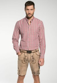 Ruitjesblouse in rood en wit met een kraag, gecombineerd met beige leren lederhosen met decoratieve stiksels en een riem met een sierlijke gesp.