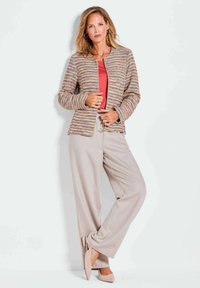 Giacca testurizzata multicolore con scollo rotondo, indossata sopra un top corallo e abbinata a pantaloni a gamba larga beige chiaro e ballerine rosa.