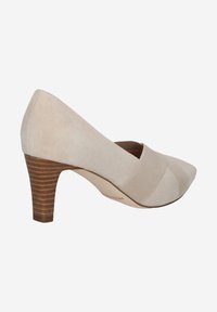 Pompe en suède beige à bout pointu, avec une bande élastique croisée et un talon en bois empilé, présentant une texture lisse et un design sans couture.