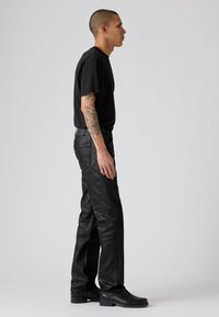 Camiseta negra y jeans oscuros de textura con un ajuste de pierna recta. Llevados con botas negras; cuenta con costuras visibles y bolsillos traseros.