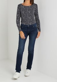 Tummansininen pitkähihaiseen paita, jossa on valkoinen kukkakuosi, yhdistettynä tummansinisiin slim fit -farkkuihin ja valkoisiin tennareihin. Sileä kangas, istuva muotoilu.