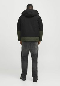Zwarte en groene gewatteerde jas met capuchon. Heeft een contrasterend ondergedeelte en gestructureerde donkergrijze jeans.