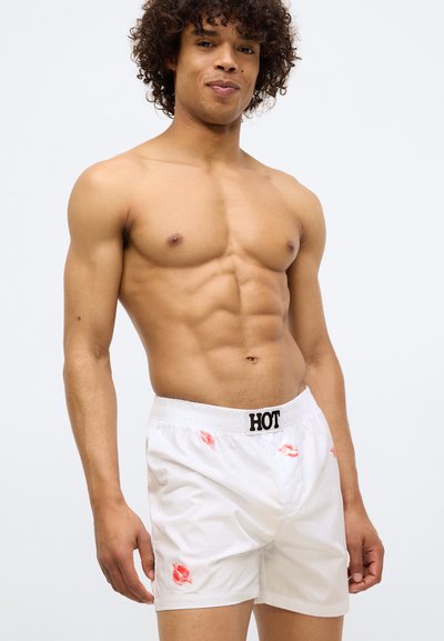 Boxeri albi cu imprimeu roșu în formă de sărut, bretele elastice cu inscripția "HOT". Material din bumbac, croi lejer, design simplu fără modele suplimentare.
