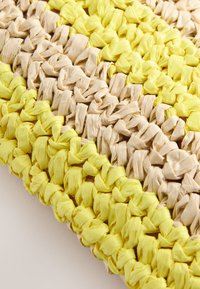 Povečani posnetek pletenine z debelo, zvozlano prejo v izmenjujočih se rumenih in bež črtah.