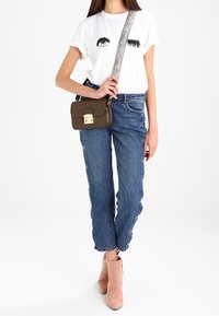 Hvid t-shirt med øje-grafik, blå denimjeans med knapdetaljer i siden og beige ankelstøvler. Brun crossbody-taske med metalspænde.