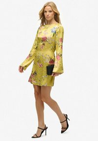Geel bloemenjurk met lange, uitlopende mouwen, van gestructureerde stof, met roze en blauwe rozen. Draag met zwarte instapheels en een gestructureerde clutch.