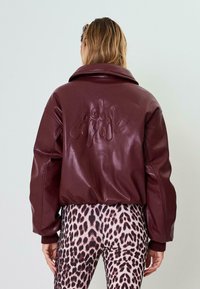 Giubbotto in ecopelle bordeaux con un grande design di testo in rilievo sulla schiena e una vestibilità comoda, abbinato a leggings con stampa leopardata.