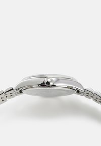 Montre en acier inoxydable argenté avec un boîtier rond, couronne texturée et bracelet à maillons. Présente une lunette lisse et un design de cadran minimaliste.