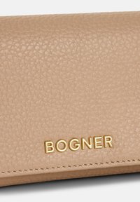 Portafoglio in pelle beige con texture, caratterizzato dal logo dorato "BOGNER" e cuciture precise lungo il bordo. Finitura liscia con una leggera lucentezza.