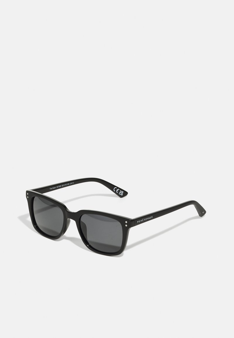 Ochelari de soare dreptunghiulari negri cu lentile închise, ramă din plastic gros și accente metalice. Prezintă text alb cu logo pe brațe și lentile gri.