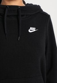 Svart huva sweatshirt gjord av mjukt material; har en känguruficka och en vit Nike-logotyp på bröstet. Justerbara snören.