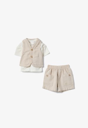 Chaleco beige abotonado sobre una camisa blanca de manga corta, combinado con pantalones cortos beige con cintura elástica y bolsillos delanteros con botones.
