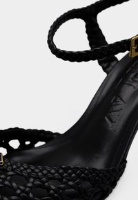 Μαύρο υφαντό δερμάτινο πέδιλο με ψηλό τακούνι, λουράκι αστραγάλου και χρυσή αγκράφα, με επένδυση εσωτερικού πέλματος με υφή και λογότυπο.