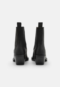 Botas de cuero negro hasta el tobillo con una textura suave, tacones apilados y tiradores en la parte posterior. Diseño minimalista sin adornos visibles.