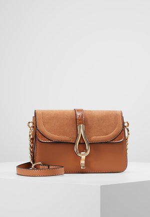 Borsa a tracolla marrone con patta in camoscio, chiusura dorata e dettaglio con catena sulla tracolla, posata su una superficie bianca con sfondo semplice.