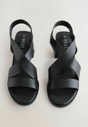 Black sandals featuring a cross-strap design, made of smooth synthetic material, with a low heel and a contoured footbed for comfort.