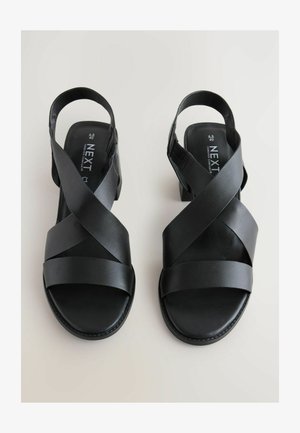 Sandali neri con un design a strappo incrociato, realizzati in materiale sintetico liscio, con tacco basso e soletta sagomata per il comfort.